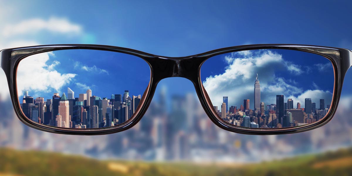 first person view staring through eye glasses at a cityscape. The image inside of the lenses is crystal clear, and the surrounding area is very blurry. This image illustrates myopia (nearsightedness), which is characterized by the inability to see clearly from a distance.